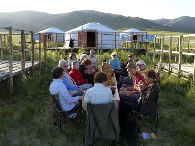 Reizigers dineren bij een gerkamp met traditionele yurts in de Mongoolse steppe, met bergen op de achtergrond.