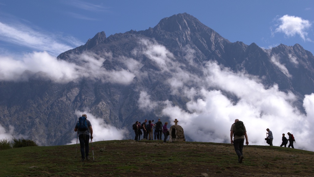 Wandelaars met rugzakken in de bergen van Armenië en Georgië, met hoge pieken en wolken op de achtergrond.