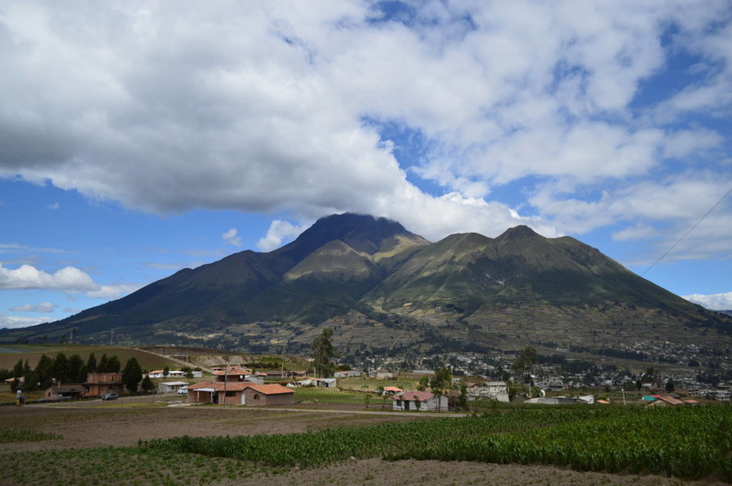 Uitzicht op de vulkaan Imbabura bij Otavalo in Ecuador, met velden en dorpjes onder een wolkenlucht.