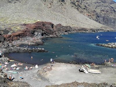 Zwart lavastrand en baai aan de kust van Tenerife, met zwemmers en boten tijdens de wandelvakantie.
