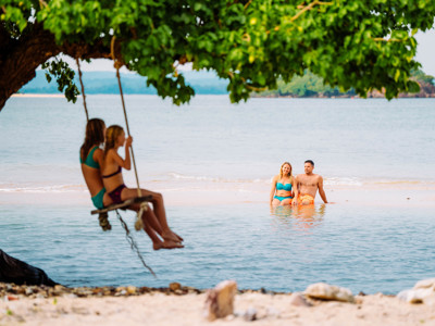Gezin ontspant op het strand in Zuid-Thailand, met kinderen op een schommel aan een boom boven zee.