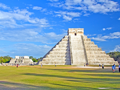 Piramide El Castillo in Chichén Itzá, Mexico, met bezoekers op het grasveld onder een blauwe lucht.