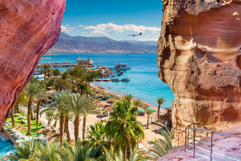 Uitzicht op Aqaba aan de Rode Zee in Jordanië, met strand, palmbomen en bergen op de achtergrond.