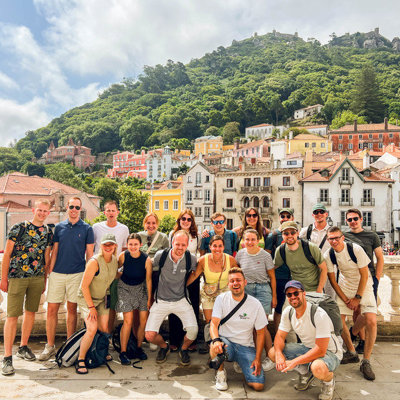 Groep 22-35ers reizigers in Sintra, Portugal, met kleurrijke huizen en groene heuvels op de achtergrond.