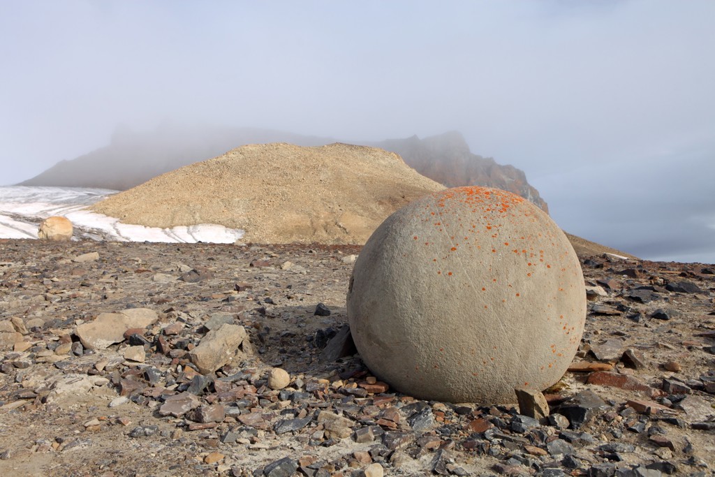 Ronde rots op een stenige kust met besneeuwde heuvels in de mist tijdens groepsrondreis Noordpool.