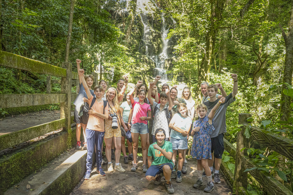 Groep gezinnen bij waterval in het regenwoud tijdens familiereis Costa Rica.