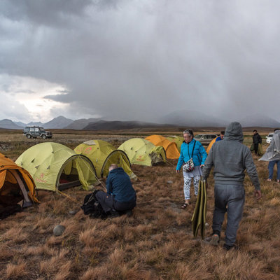 Kampeerplek met tenten en reizigers in Baltistan, Pakistan, onder donkere regenwolken in berglandschap.