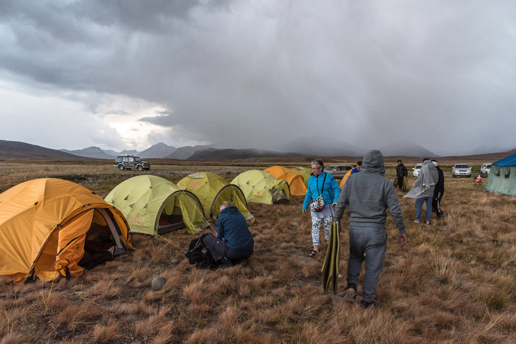 Kampeerplek met tenten en reizigers in Baltistan, Pakistan, onder donkere regenwolken in berglandschap.