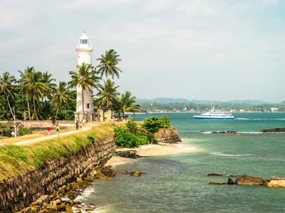 Witte vuurtoren bij Galle Fort aan de kust van Sri Lanka, met palmbomen en een boot op zee.