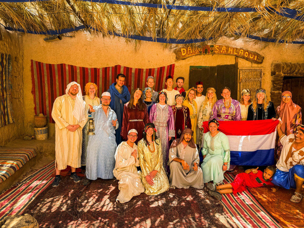 Groepsfoto van 22-35ers reis Marokko in traditionele kleding bij een woestijnkamp.