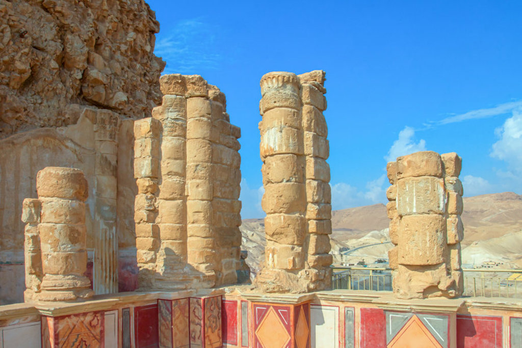 Ruïnes met stenen zuilen op Masada in Israël, met uitzicht op de woestijn onder een heldere blauwe lucht.
