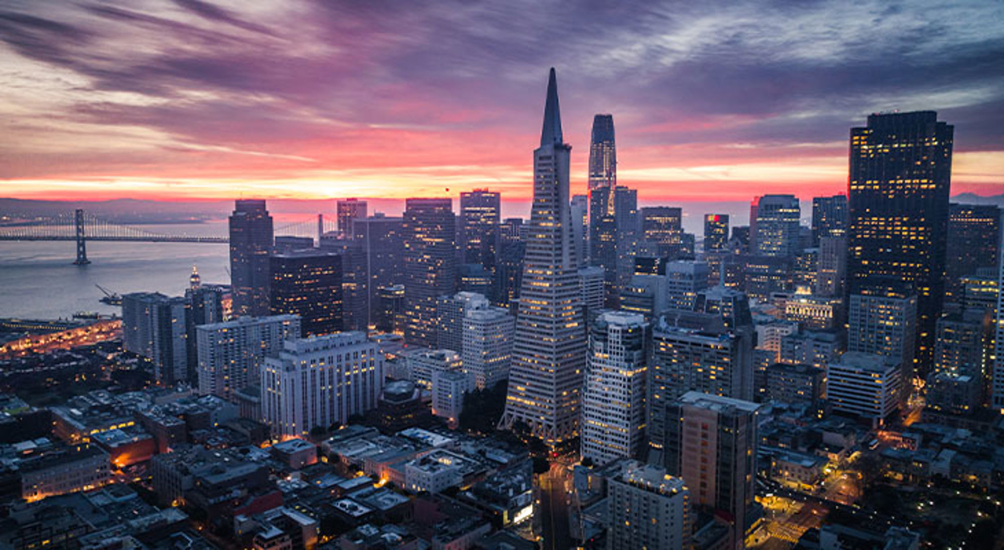 San Francisco Skyline van San Francisco bij zonsondergang met de Transamerica Pyramid en de Bay Bridge op de achtergrond.