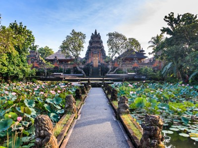 Lotusvijver met stenen beelden en pad naar een Balinese tempelcomplex in Ubud, Bali.