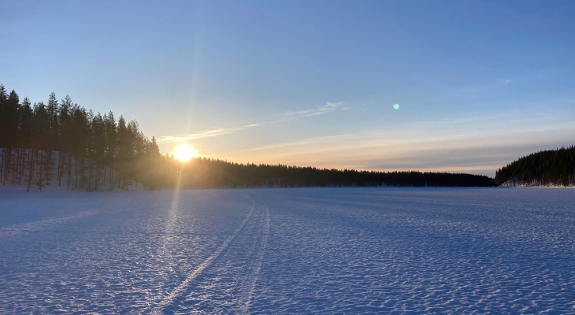 Fins Lapland Zonsondergang boven een bevroren meer met sneeuw en een bosrand op de achtergrond.