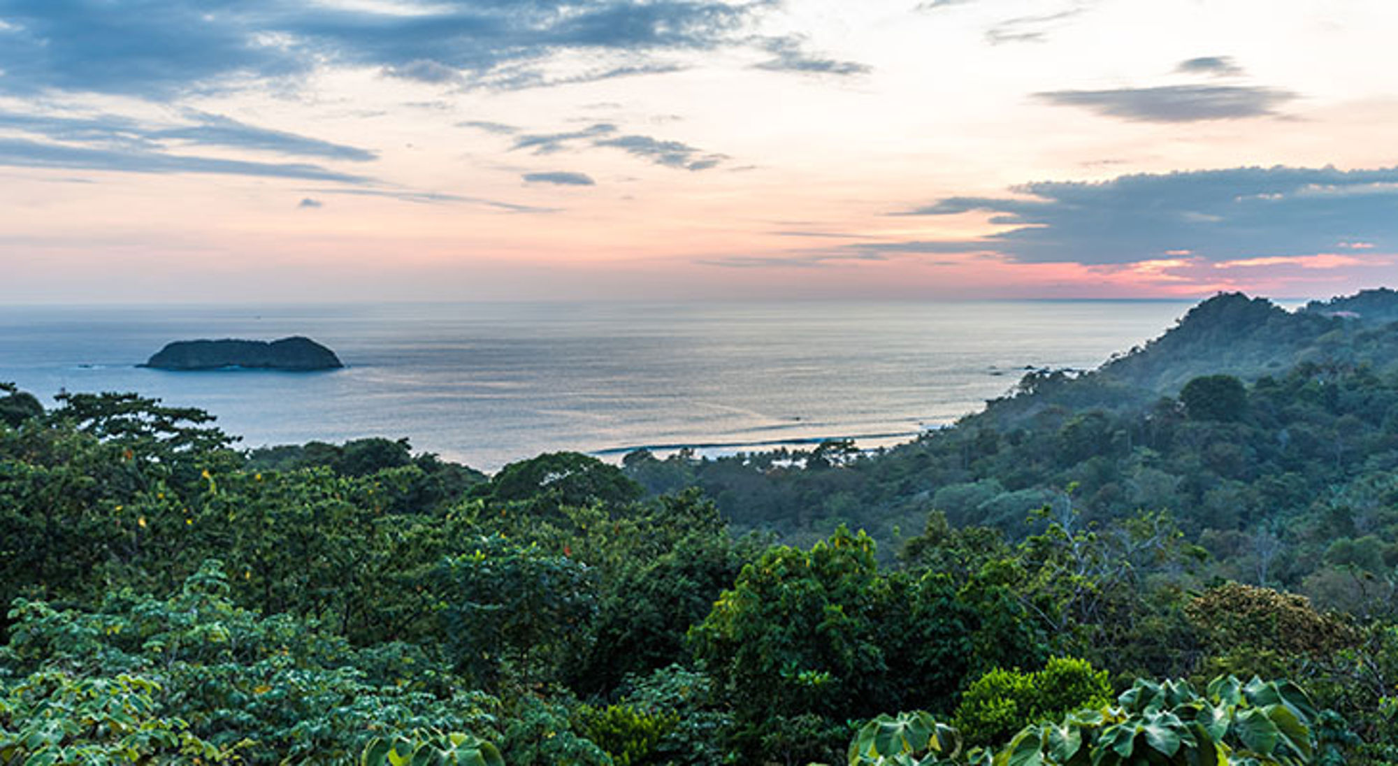 Uitzicht over de kustlijn en zee bij zonsondergang in Costa Rica, met groen regenwoud op de voorgrond.