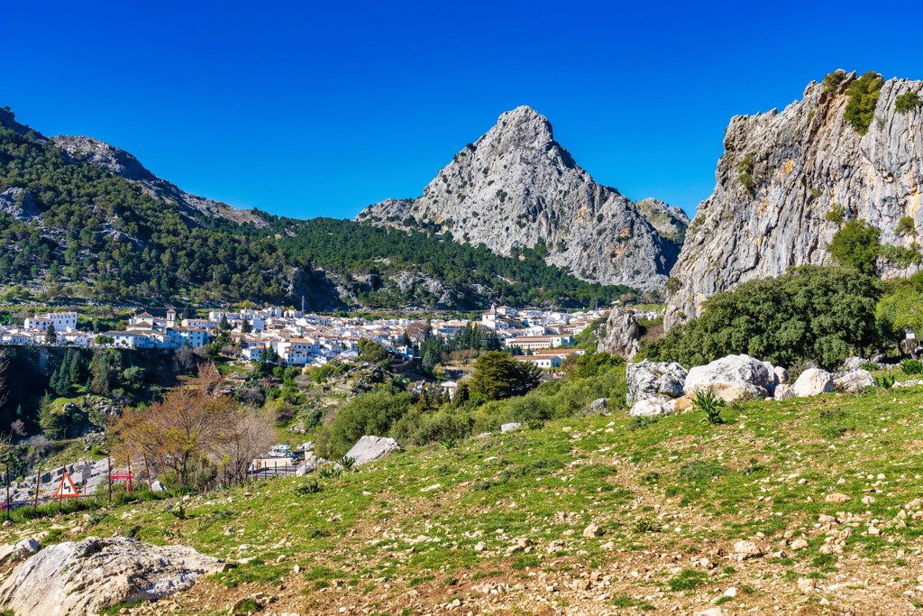 Wit Andalusisch bergdorp in Spanje, omringd door rotsen en groene heuvels onder een blauwe lucht.