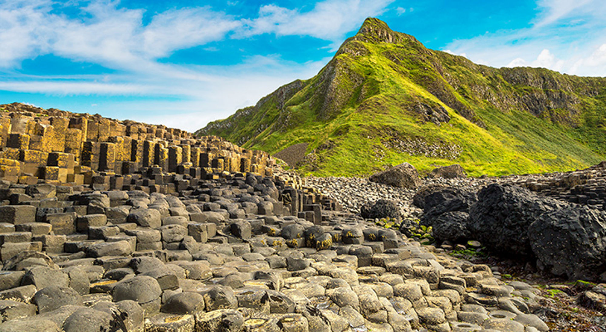Giant's Causeway, Noord-Ierland Basaltzuilen van Giant’s Causeway aan de kust van Noord-Ierland, met groene heuvels op de achtergrond.