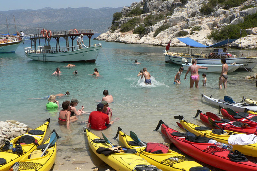 Gezinnen zwemmen en kajakken in een baai aan de kust van Zuid-Turkije, met bootjes voor anker.