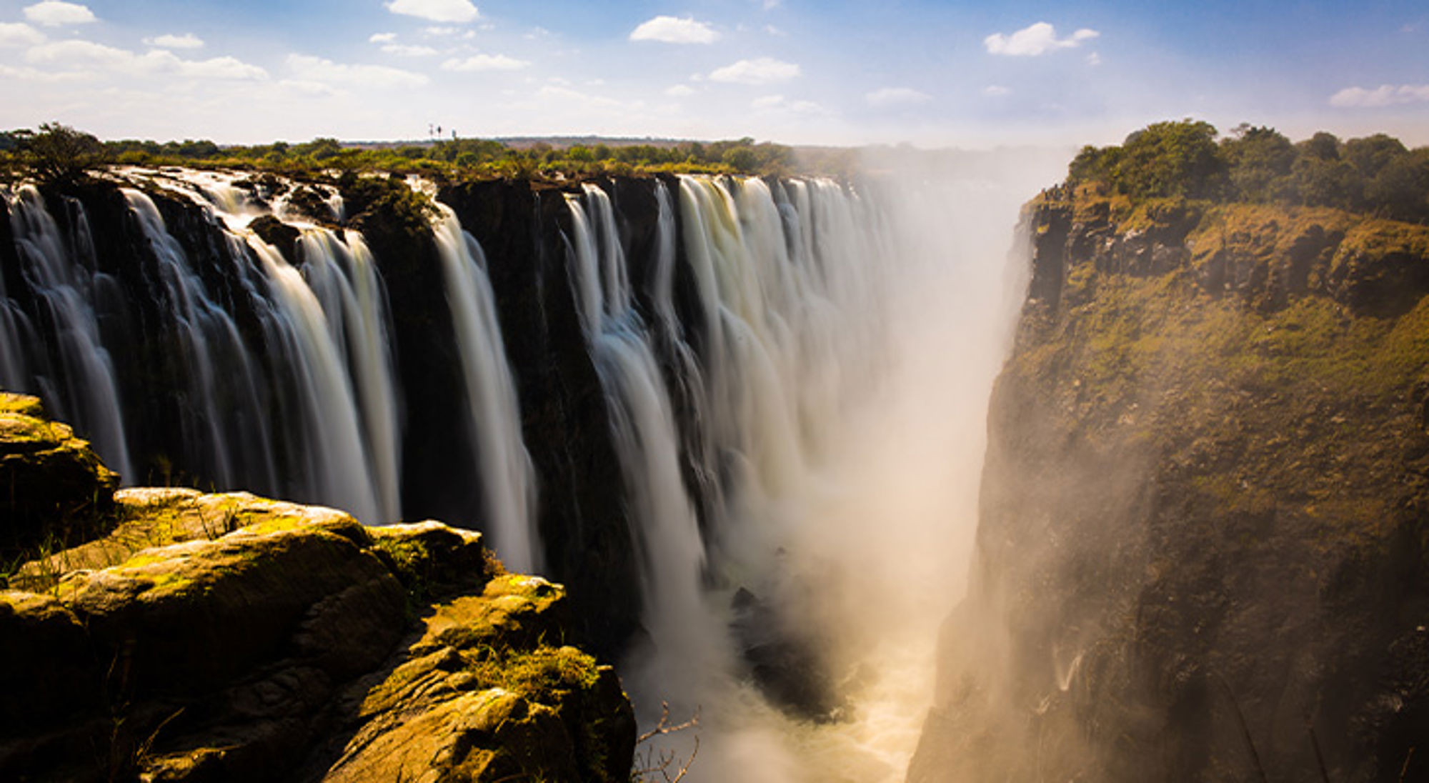 Victoria Falls - Zimbabwe Uitzicht op de Victoriawatervallen met nevel boven de kloof en watervallen langs de rotsrand.