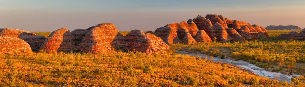 Zonsondergang bij de Bungle Bungle Range in West-Australië, met roodgelaagde rotskoepels en rivierbedding.