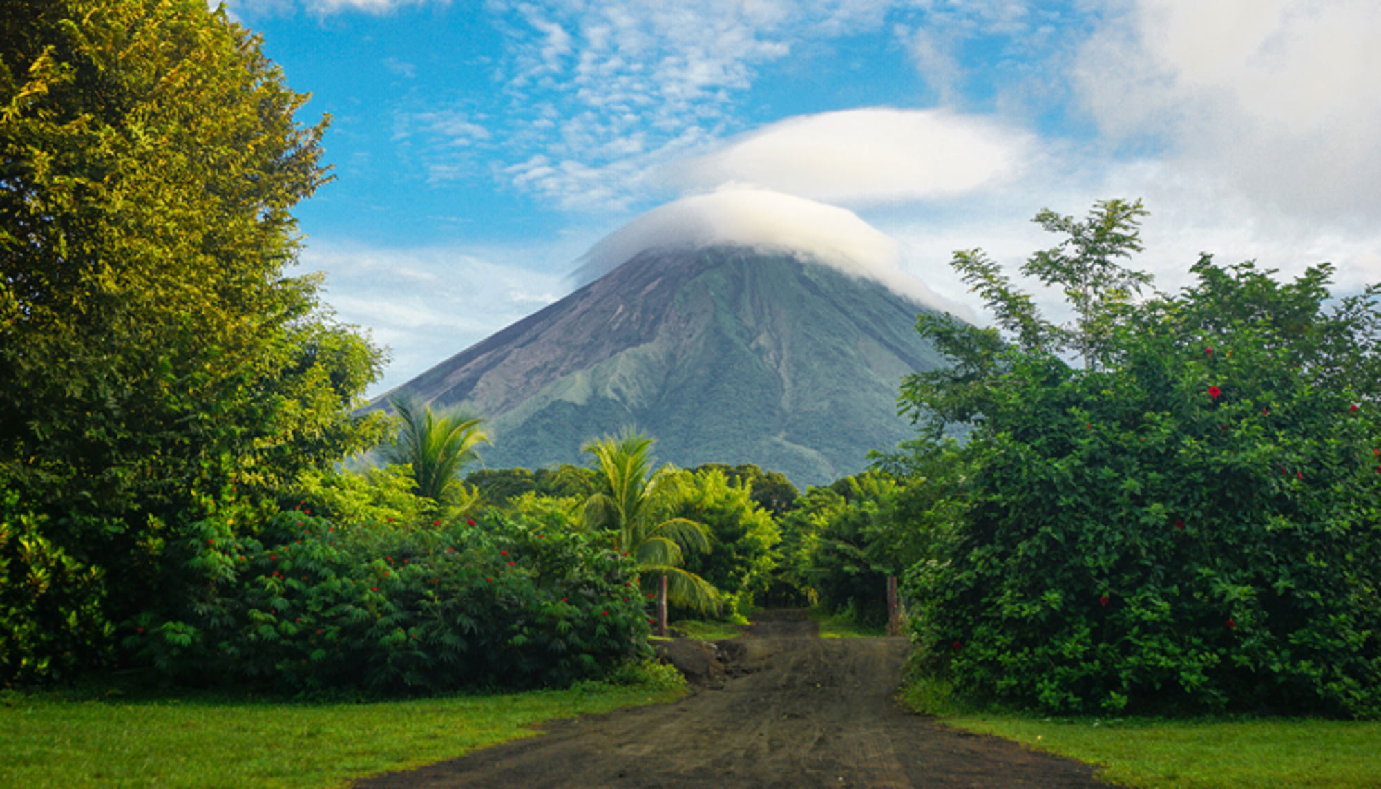 Vulkaan Arenal met wolken rond de top, gezien vanaf een pad door tropisch groen in Costa Rica.