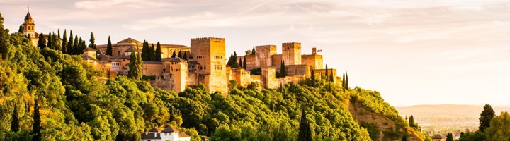 Alhambra in Granada, Andalusië, met paleis en torens boven groene heuvels in avondlicht.