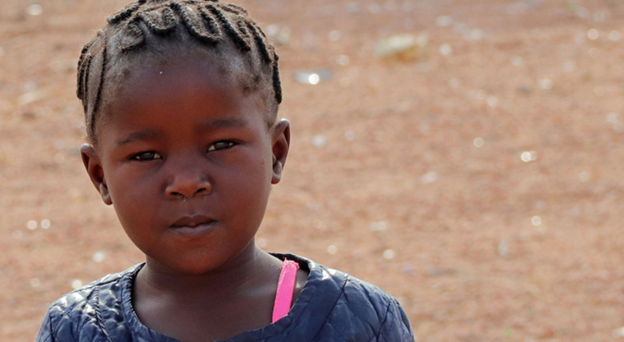 lokaal meisje in herero dorp in namibie Portret van een jong meisje met ingevlochten haar, staand buiten op een zandige ondergrond.