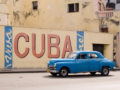 Blauwe klassieke auto rijdt langs muurschildering met het woord Cuba in Havana.