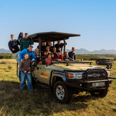 Familiereis Zuid-Afrika: groep in safarijeep tijdens game drive, met bergen op de achtergrond.