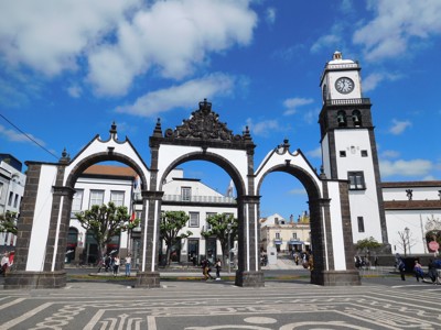 Stadspoort Portas da Cidade in Ponta Delgada op São Miguel, Azoren, met klokkentoren en blauw wolkendek.