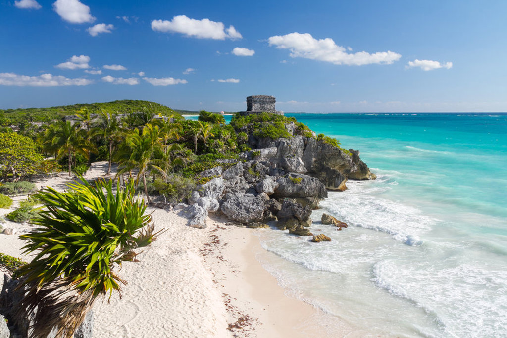 Maya-ruïnes van Tulum aan een wit zandstrand met palmen en turquoise zee in Mexico.