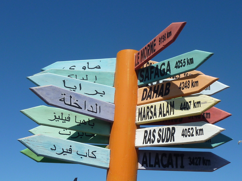 Gekleurde wegwijzer met bestemmingen in Arabisch en Engels tegen een blauwe lucht tijdens een familiereis Marokko zomer.