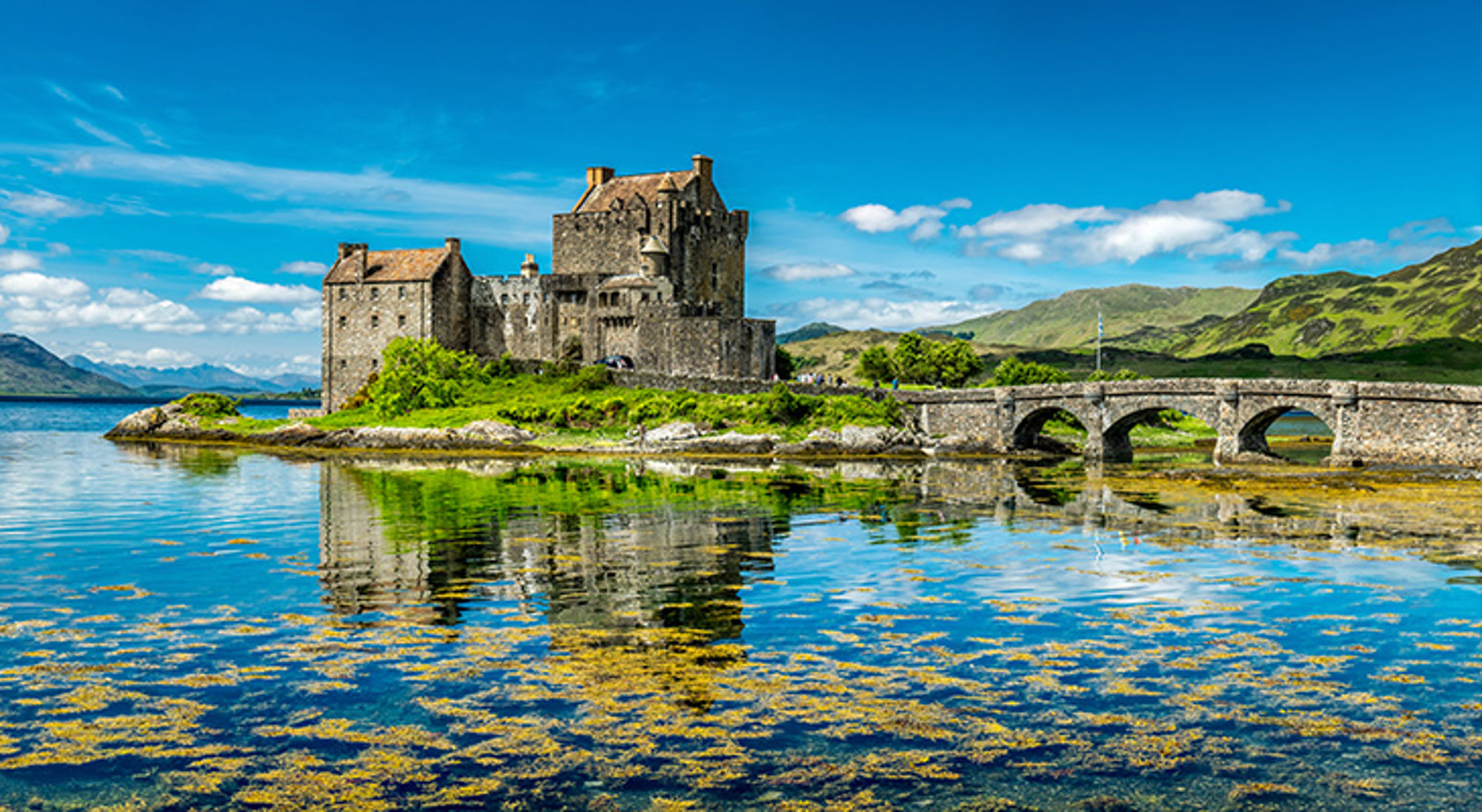 Eilean Donan Kasteel in Schotland Eilean Donan Castle met stenen brug weerspiegeld in het water, met bergen op de achtergrond.