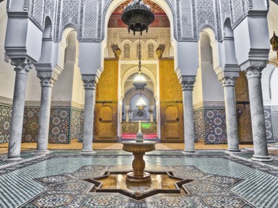 Rijk versierde binnenplaats van een Marokkaanse riad met mozaïektegels, zuilen en fontein.
