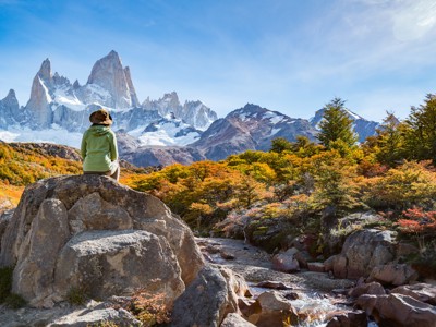 Wandelaar kijkt uit op de Fitz Roy-berg in Patagonië, met besneeuwde pieken en herfstbos.