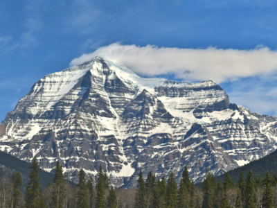 Sneeuwbedekte bergtop in de Canadese Rockies langs de Route Canada, met dennenbos en blauwe lucht.