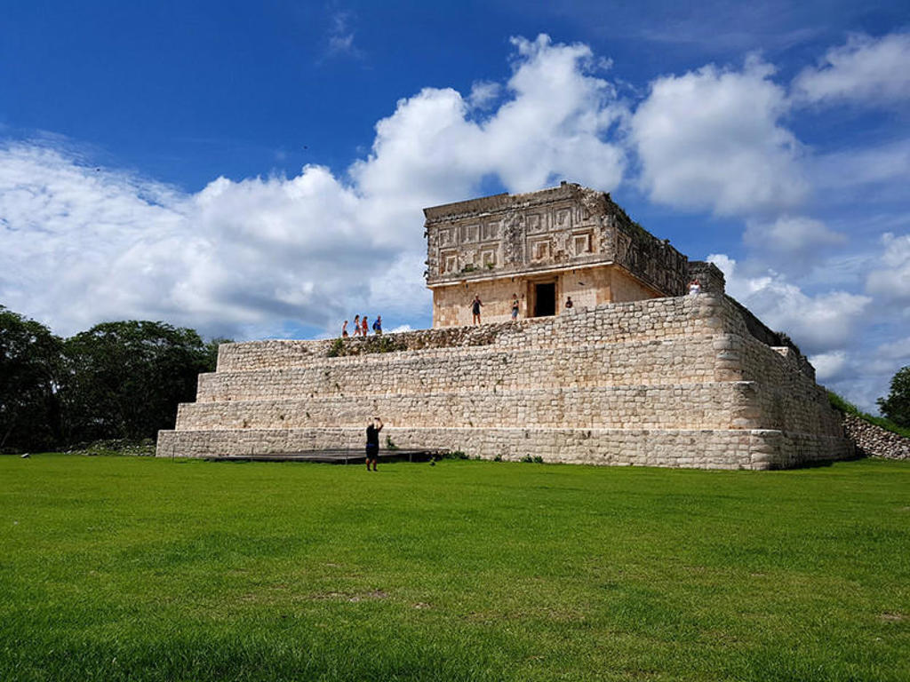 Maya-tempel in Uxmal, Mexico, met bezoekers op het terras onder een blauwe lucht.
