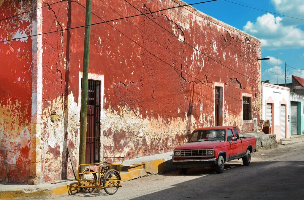 Rode pickup geparkeerd langs een verweerde rood-witte gevel in Mexico, tijdens de Groepsrondreis Mexico Chill & Adventure.