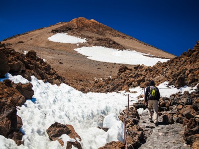 Wandelaar op rotsachtig pad langs sneeuwvelden op de Teide, Tenerife.