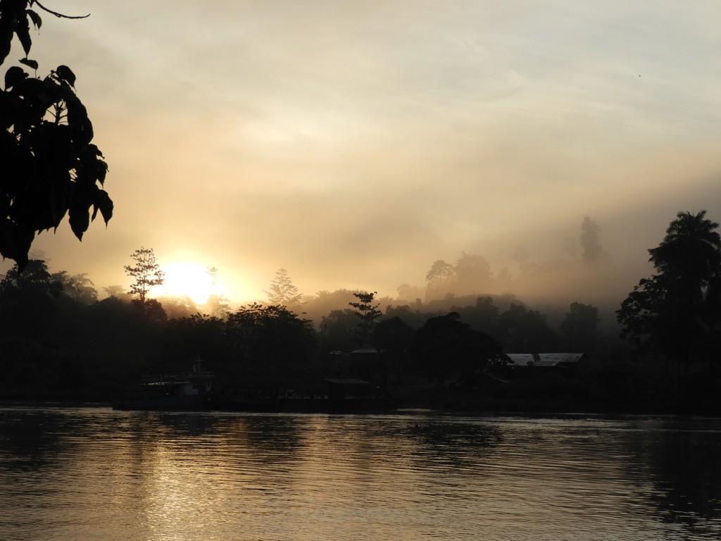 Zonsopkomst boven een mistige rivier in Maleisisch Borneo, met silhouetten van jungle en bomen.