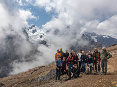 Groep wandelaars op een bergpad in Peru met besneeuwde Andes-toppen op de achtergrond.