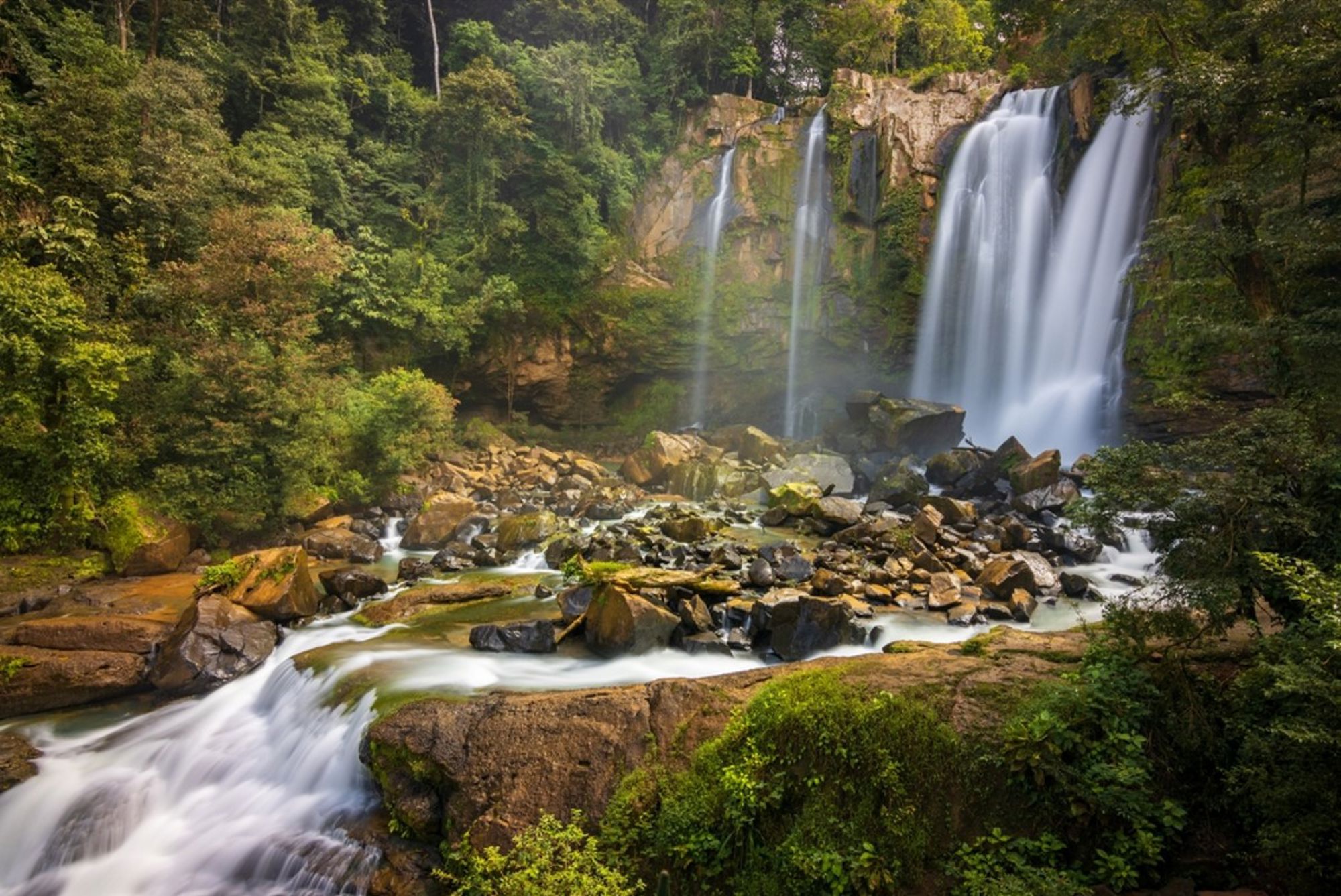 Waterval in het regenwoud van Costa Rica met rotsen en een snelstromende rivier.