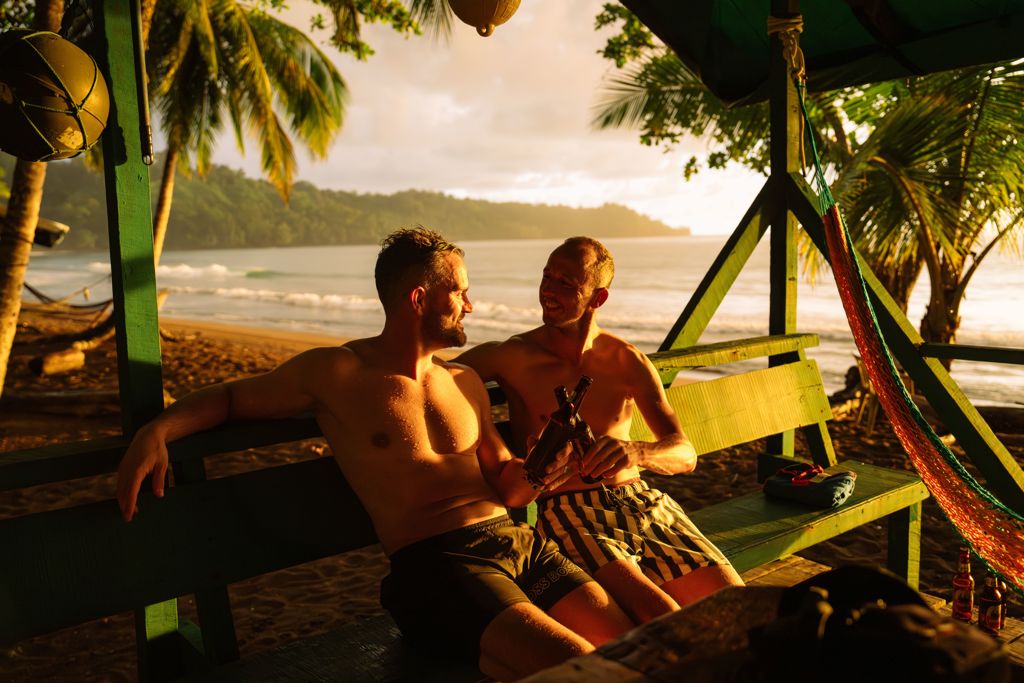 Twee vrienden ontspannen met een drankje op een bankje aan het strand in Costa Rica bij zonsondergang.