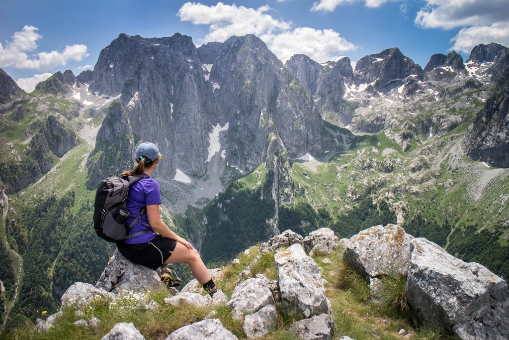 Wandelaar met rugzak kijkt uit over de Peaks of the Balkan met steile bergtoppen en sneeuwvelden.