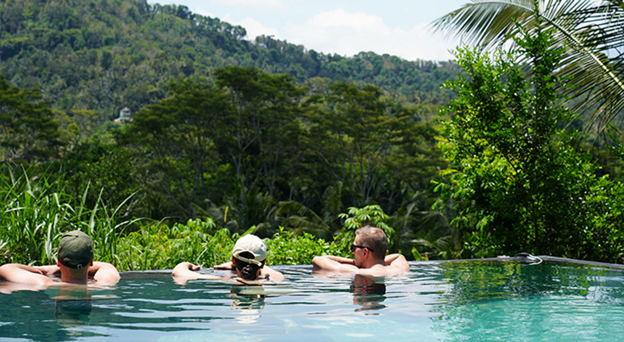 Sidemen Bali Drie reizigers ontspannen in een infinitypool met uitzicht op een groene jungle en heuvels.