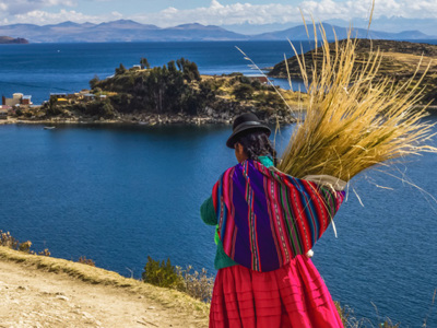 Vrouw in traditionele kleding met riet op haar rug bij het Titicacameer in Peru.