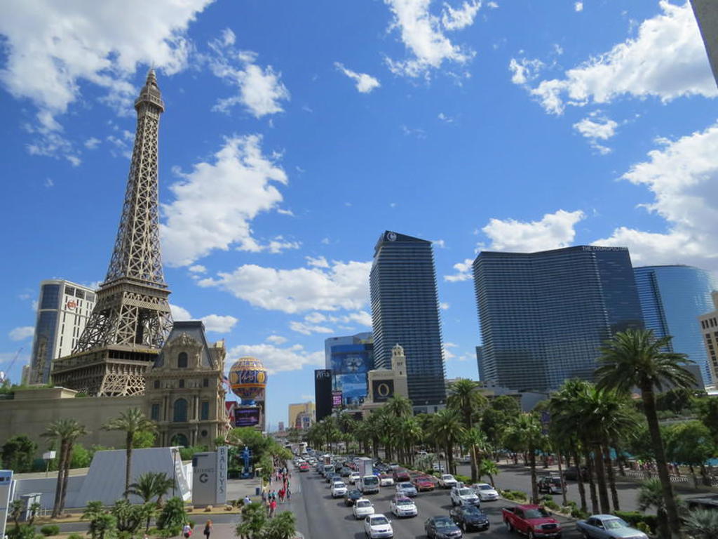 Las Vegas Strip met de Eiffeltoren van Paris Las Vegas, palmbomen en moderne hotels onder een blauwe lucht.