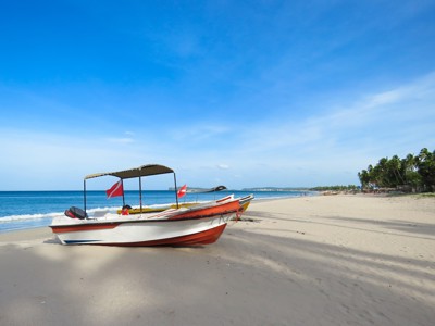 Vissersboot op een wit zandstrand aan de kust van Sri Lanka, met palmbomen en helderblauwe lucht.