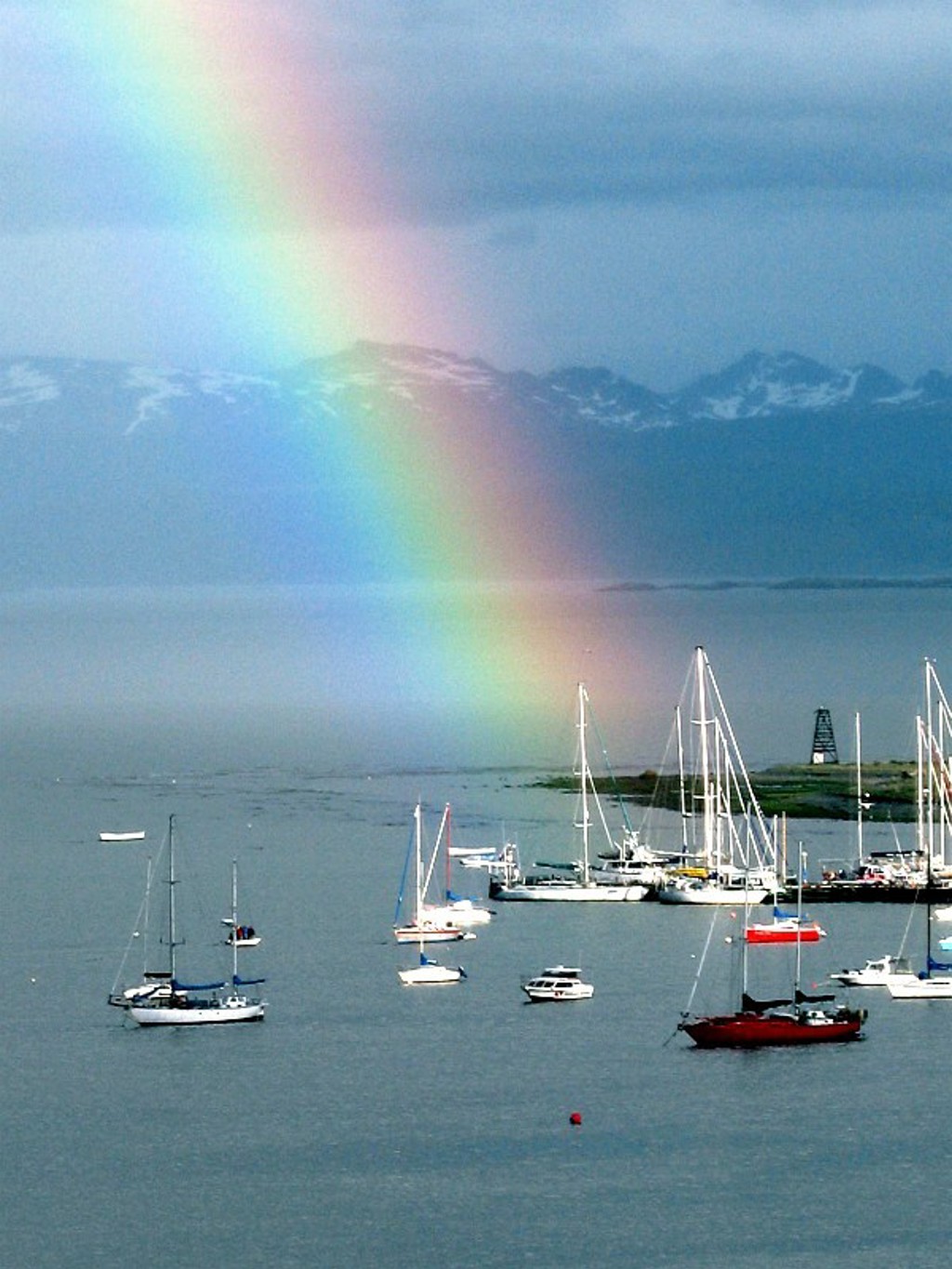 Regenboog boven de haven met zeilboten en besneeuwde bergen in Patagonië, Argentinië.