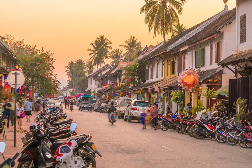 Drukke straat in Luang Prabang met koloniale huizen, palmbomen en scooters tijdens een familiereis Thailand, Laos en Cambodja.